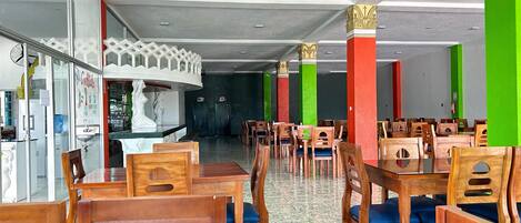 Un restaurant avec des chaises et des tables en bois, un comptoir orné d’une statue blanche et des piliers aux couleurs vives.