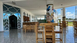 A spacious hall with wooden benches and a marble floor, large windows, and a decorative column with figures. - Hotel Palace (Independencia)