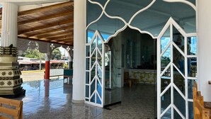 A covered outdoor area with tiled flooring, a wooden bench, and a decorative column. - Hotel Palace (Independencia)