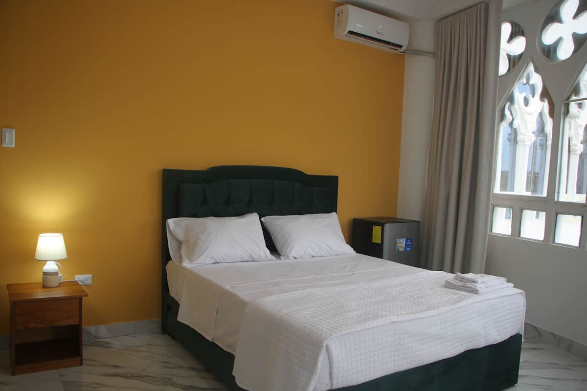 A hotel room with a bed, a nightstand with a lamp, a dresser, and a window with curtains.