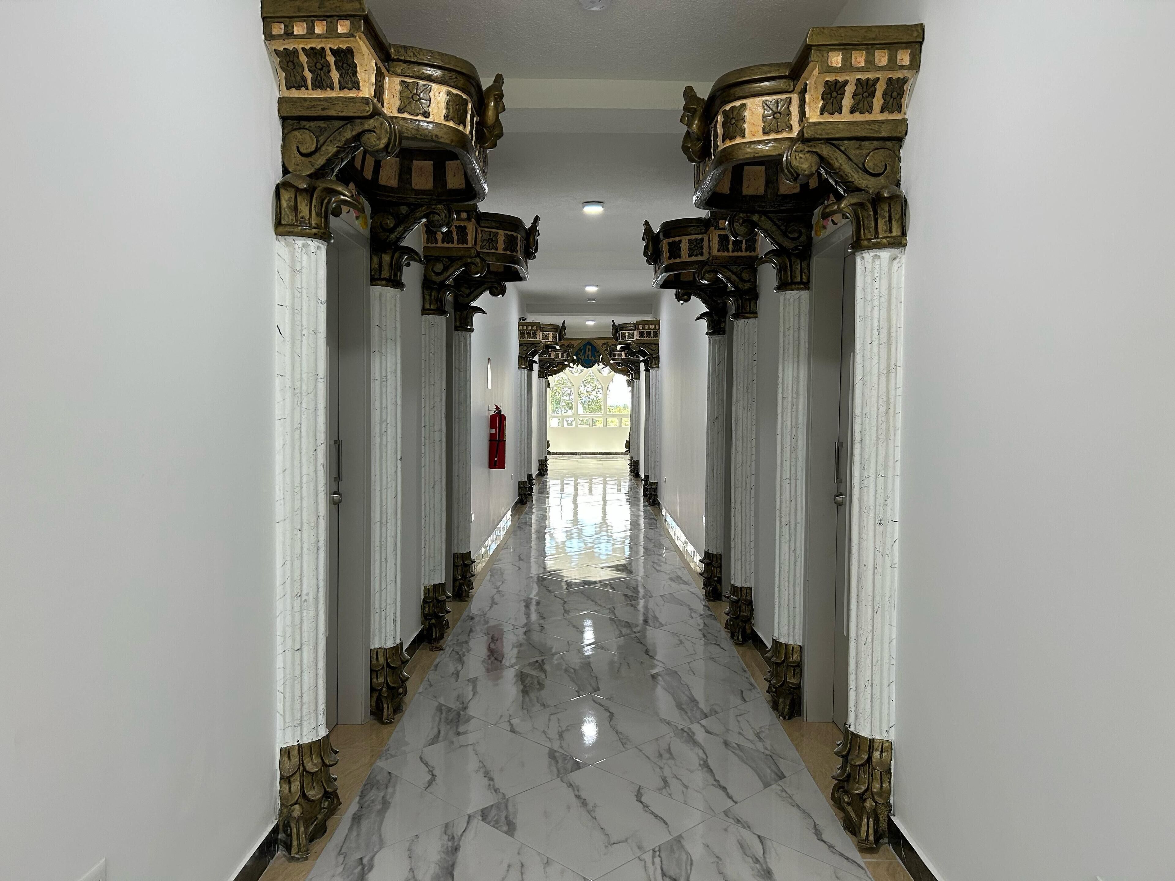 Un pasillo con suelo de mármol y columnas ornamentadas de color oscuro.