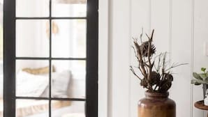 Una mesa de madera rústica con un florero de ramas secas, una silla y una puerta con diseño de cuadrícula.