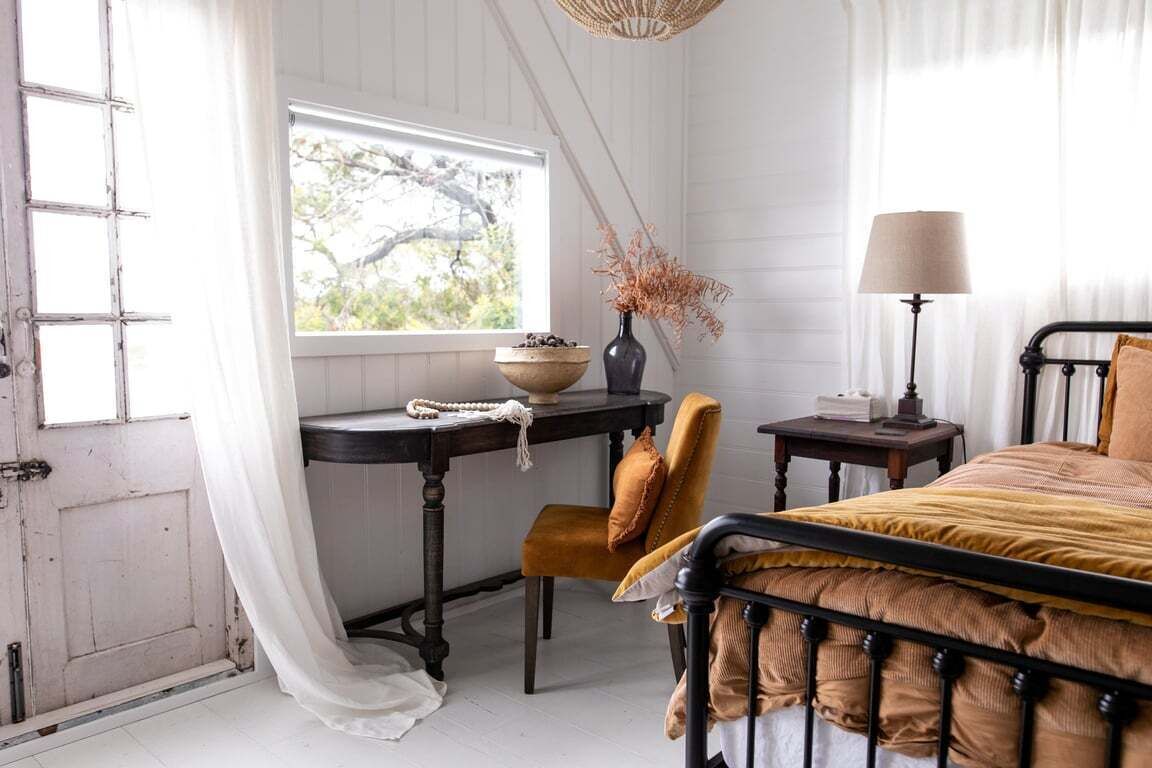 Une chambre à coucher avec un lit, une chaise, une table ornée d’un vase et une fenêtre donnant sur un beau paysage.