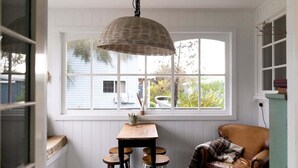Una habitación acogedora con un ventanal grande, una mesa de madera con taburetes, una silla y una lámpara colgante.