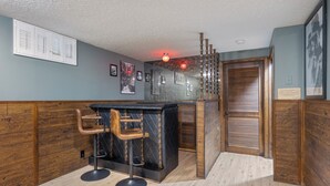 Een bar met een zwarte toonbank, twee barkrukken en een houten wand.