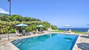 A swimming pool with lounge chairs and umbrellas, surrounded by lush greenery and a view of the ocean. - Charming oceanfront 2-bedroom condo with WiFi, AC, 2 Lanais, walk to beach! (Princeville)