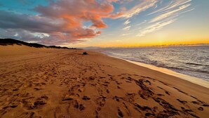 A beach with footprints leading to the water, a clear sky, and distant mountains. - Charming oceanfront 2-bedroom condo with WiFi, AC, 2 Lanais, walk to beach! (Princeville)