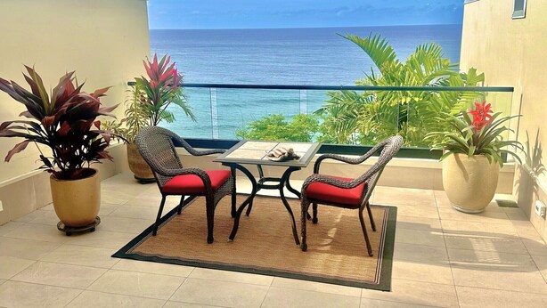 A balcony with a table and chairs, potted plants, and a view of the ocean. - Charming oceanfront 2-bedroom condo with WiFi, AC, 2 Lanais, walk to beach! (Princeville)