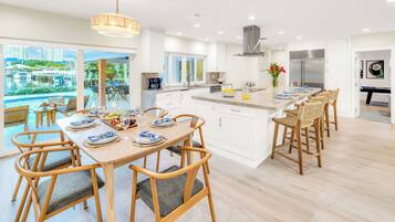 Une cuisine moderne avec des meubles blancs, un îlot central et un coin repas comprenant des chaises en bois et une table dressée pour six personnes.