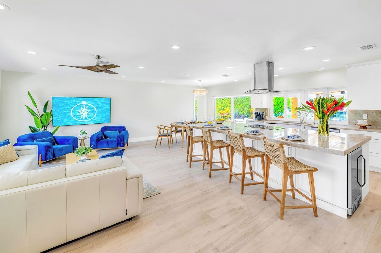 Une cuisine moderne dotée d’un îlot central, de tabourets de bar et d’un coin repas avec un canapé blanc et des chaises bleues.