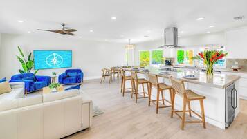 Une cuisine moderne dotée d’un îlot central, de tabourets de bar et d’un coin repas avec un canapé blanc et des chaises bleues.