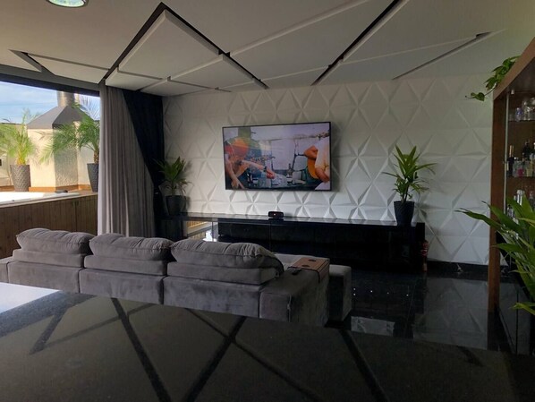 Una sala de estar moderna con un sofá modular, un televisor de pantalla plana montado en una pared con textura y una mesa de centro de vidrio.