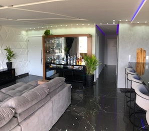 Una sala de estar moderna con un sofá gris, una zona de bar con botellas y una planta.