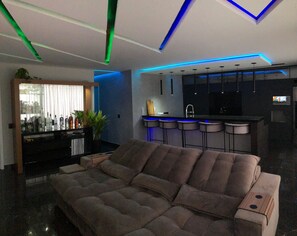 Una sala de estar moderna con un sofá seccional, una zona de bar con taburetes y una cocina con encimera negra.