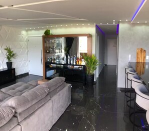 A modern living room with a grey sectional sofa, a glass coffee table, and a bar area with a mirrored backsplash. - Residencial Beach Palace (Florianopolis)