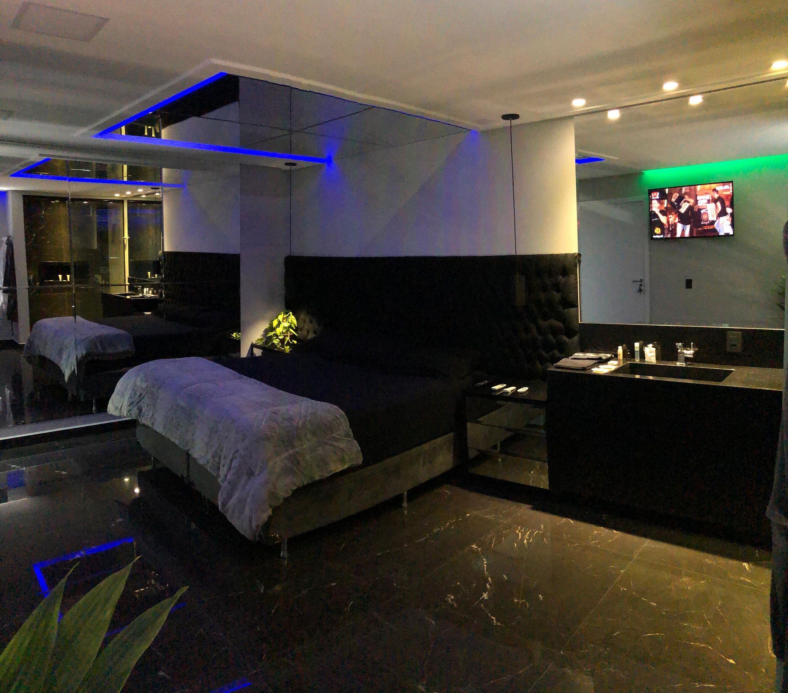 Un dormitorio moderno con una cama grande, una mesita de noche, un espejo y un televisor montado en la pared.