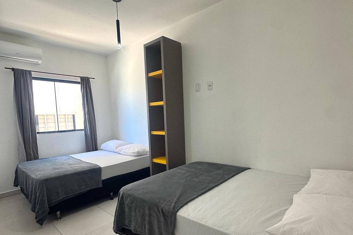 Habitación de hotel con dos camas, un armario y una ventana con cortinas.