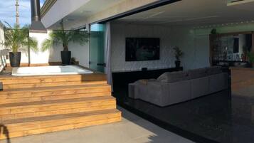 Un área exterior moderna para disfrutar del aire libre, con un jacuzzi, escalones de madera, una zona de estar con sofá y un televisor montado en la pared.