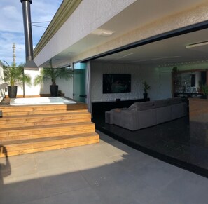 A modern outdoor living area with a hot tub, wooden steps, a seating area with a sofa, and a TV mounted on the wall. - Residencial Beach Palace (Florianopolis)