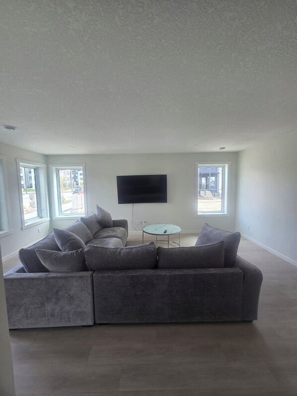A spacious living room with a sectional sofa, a flat-screen TV, and a small coffee table. - Tranquil 3-bedroom house with WiFi in Calgary Livingston (Calgary)