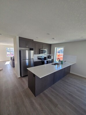 A modern kitchen with dark cabinets, stainless steel appliances, and a large island. - Tranquil 3-bedroom house with WiFi in Calgary Livingston (Calgary)