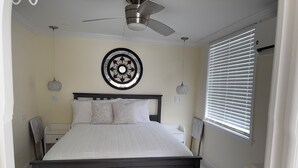 Un dormitorio con una cama de madera oscura, un ventilador de techo, un plato decorativo en la pared y una ventana con persianas.