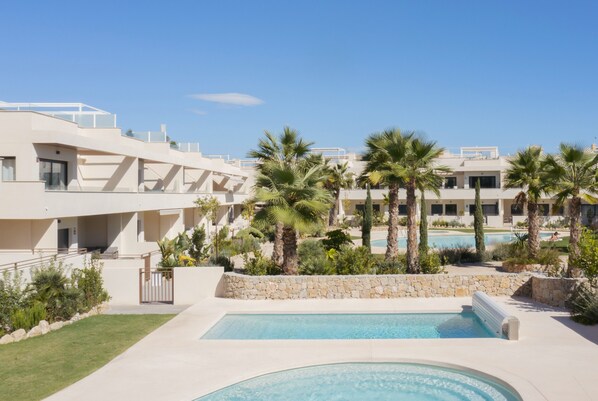 Ein modernes Hotel mit Pool, Palmen und blauem Himmel.