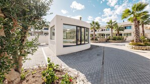 A modern building with large windows, surrounded by palm trees and a paved area. - Mediterranean Gardens 35: Top floor sea views (Torrevieja)