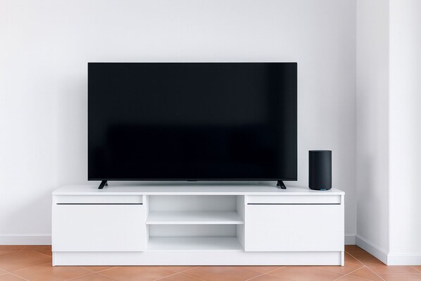Un televisor de pantalla plana sobre un mueble blanco para entretenimiento, con un altavoz negro a su lado.