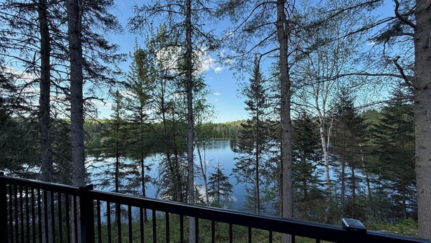 A deck with a view of a lake surrounded by tall trees. - Welcome to your haven of peace, a magnificent chalet nestled in the heart of nature. (Rivière-Rouge)