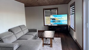 A living room with a grey sectional sofa, a wooden coffee table, and a flat-screen TV on a stand. - Welcome to your haven of peace, a magnificent chalet nestled in the heart of nature. (Rivière-Rouge)