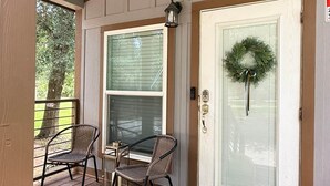 A porch with two wicker chairs, a ceiling fan, and a door with a wreath.