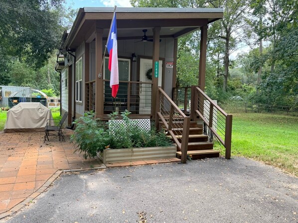 A small building with a porch, a flag, and a staircase leading up to a door. - The Refuge @ Vanderosa (Conroe)