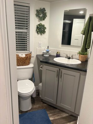 A compact bathroom with a toilet, sink, and cabinets. - The Refuge @ Vanderosa (Conroe)