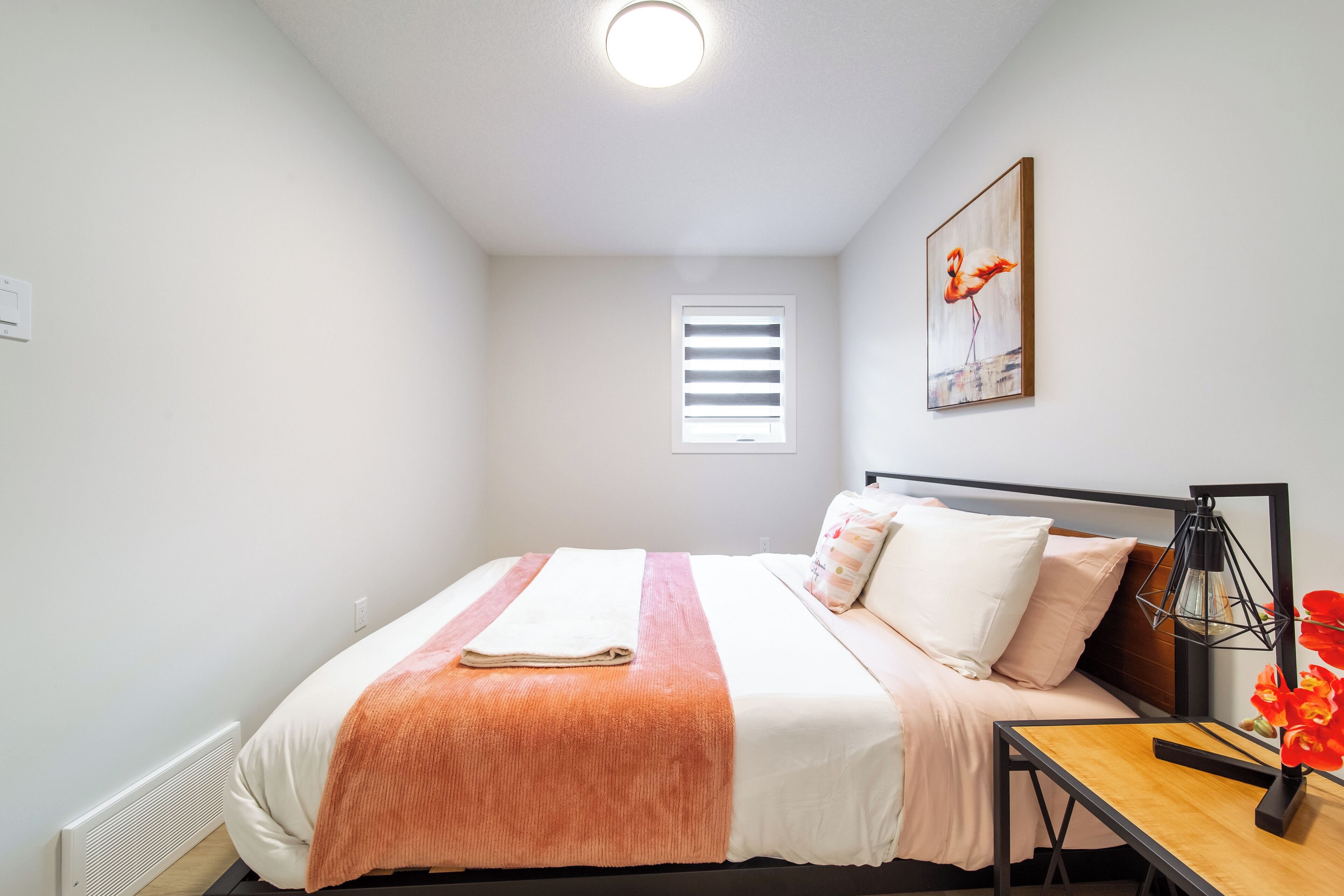 A neatly arranged bedroom with a bed, bedside table, lamp, and a window with blinds.