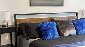 Un dormitorio ordenado con una cama, una mesita de noche con lámpara y un cuadro colgado en la pared.