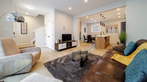 Una sala moderna con una mesa de centro de vidrio, un sofá de cuero y una zona de comedor con una cocina al fondo.