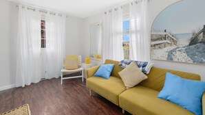 A living room with a yellow sofa, a chair, and a painting of a beach scene.
