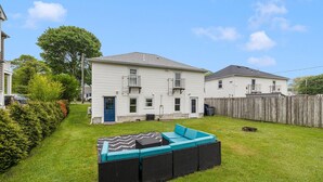 A residential backyard with a grassy lawn, a wooden fence, and a black outdoor sofa with teal cushions.