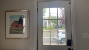 A room with a door leading to a street view, a framed painting on the wall, and a visible light switch.