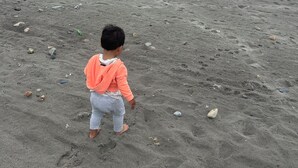 A child on a sandy beach with scattered rocks and the ocean in the background.