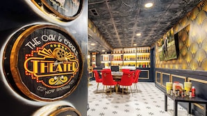 A bar area with a neon sign, red chairs, and a patterned floor.