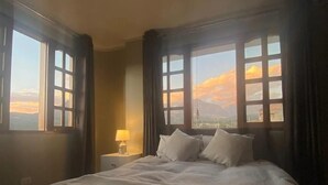 Une chambre d’hôtel avec un grand lit, deux tables de chevet et une vue sur les montagnes par les fenêtres.