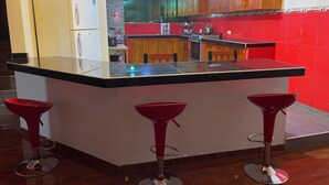 Une cuisine dotée d’un îlot central, de meubles en bois, d’un pare-feu rouge et de trois tabourets de bar rouges.