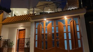 A two-story building with a large wooden gate, a balcony with a metal railing, and a tiled roof. - Lodging "YURAQ WASI" - Huaraz (Independencia)