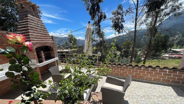 Un espace patio agrémenté d’une cheminée en briques, de meubles en osier et offrant une vue sur un paysage montagneux.