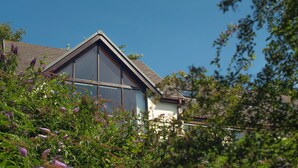 A modern house with large windows and a sloped roof, surrounded by lush greenery. - Rhyd y Groes Bach, Holiday Cottage Burton, Sleeps 6, 3 bedrooms,  bathrooms (Milford Haven)