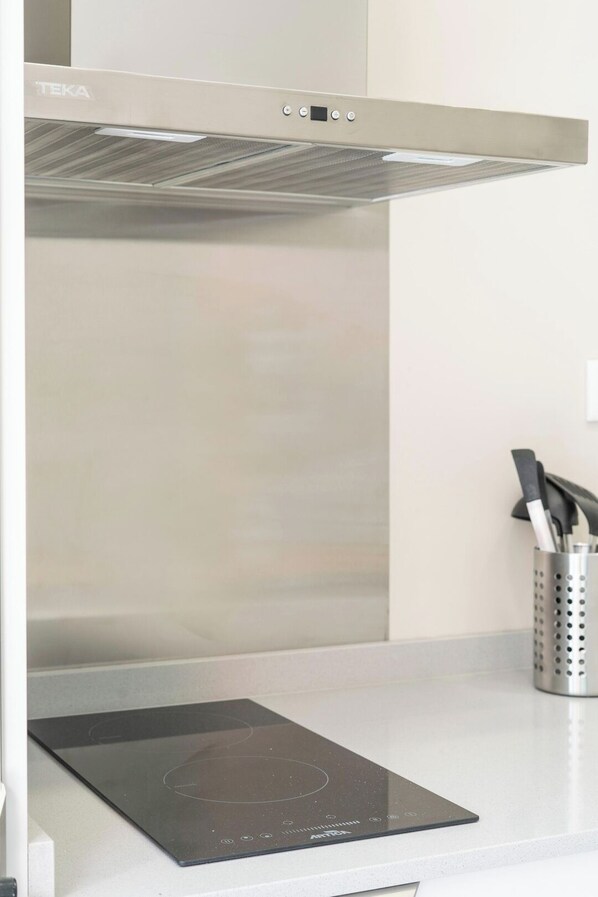 A kitchen with a stainless steel range hood, a black induction cooktop, and a stainless steel utensil holder.