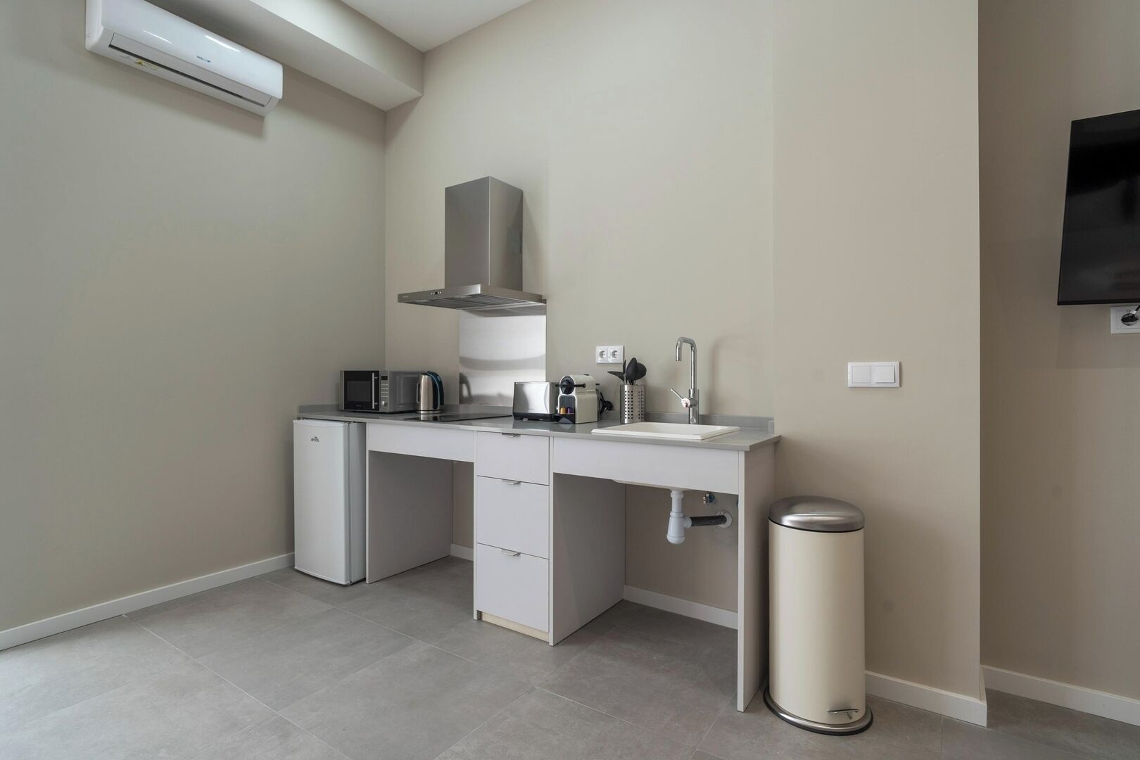 Eine kompakte Küche mit integriertem Mikrowellenherd, Toaster und Wasserkocher, einem kleinen Kühlschrank, einer Spüle mit modernem Wasserhahn und einem Mülleimer.