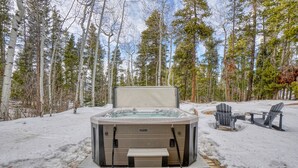 A hot tub in a snowy forest setting with a stone bench and Adirondack chairs. - MountainTop Mega A Frame Chalet with Hot Tub (Black Hawk)